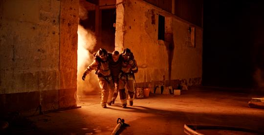 Firefighters taking an injured firefighter out of a burning building